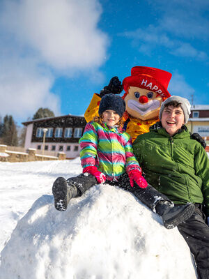 Familienhotel Mein Krug im Fichtelgebirge: Kinder im Schnee mit dem Maskottchen Happy. Sie sitzen auf einem großen Schneeball